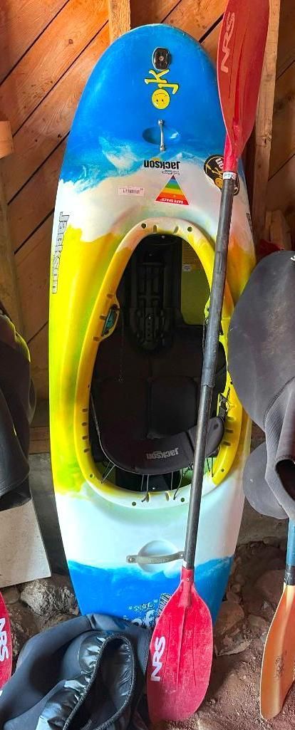 A colorful kayak with a paddle inside a shed.
