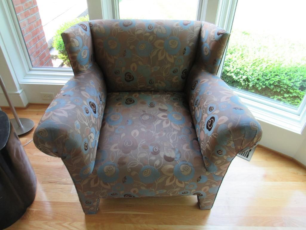 Upholstered armchair with floral pattern; by a window on wooden floor.