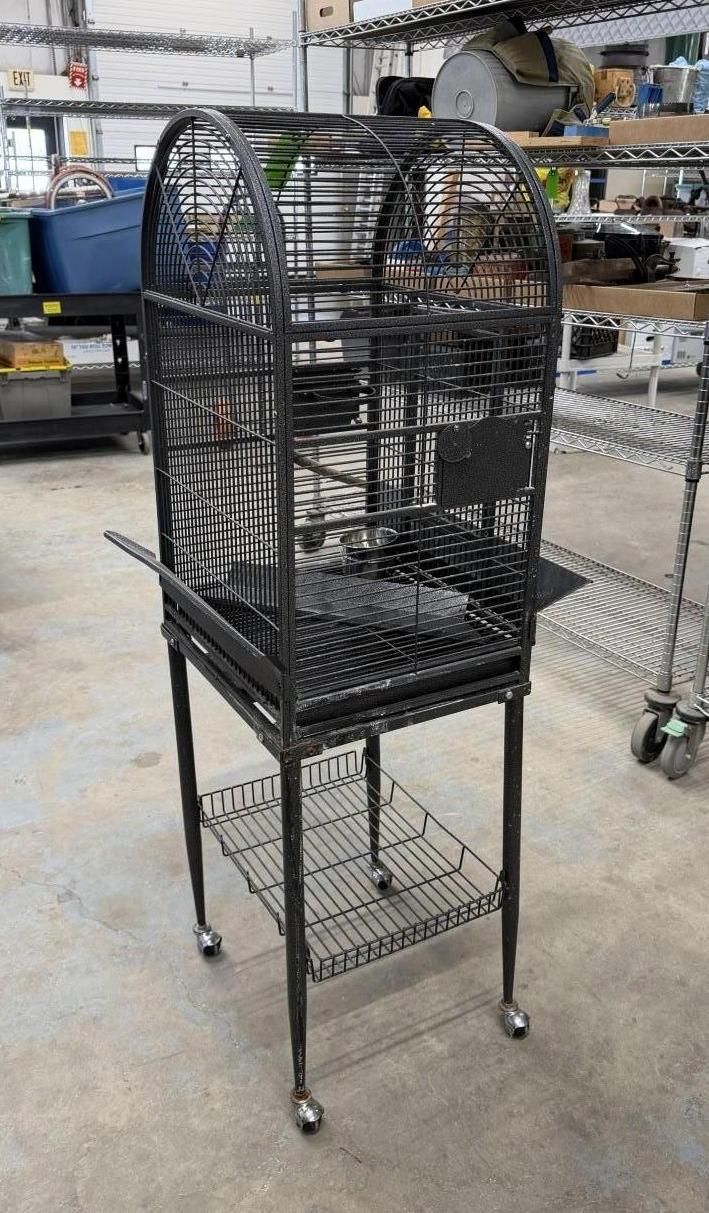 Black metal bird cage on a rolling stand, with a curved top and interior wire mesh.