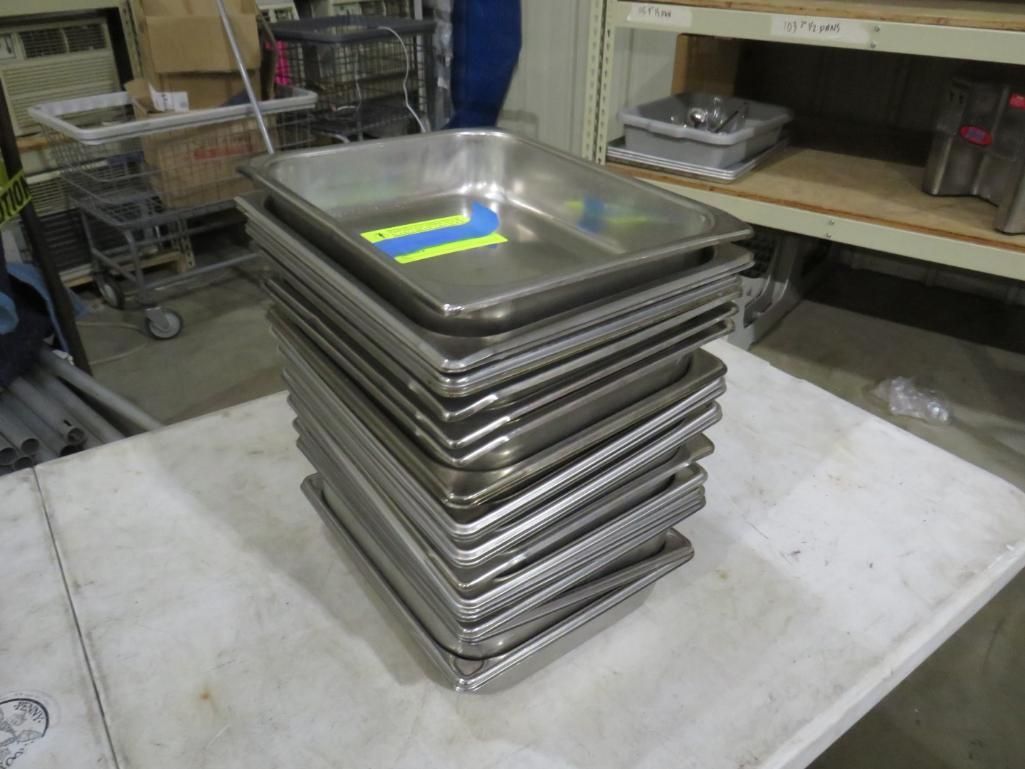 Stack of stainless steel food trays on a white table in a storage area.