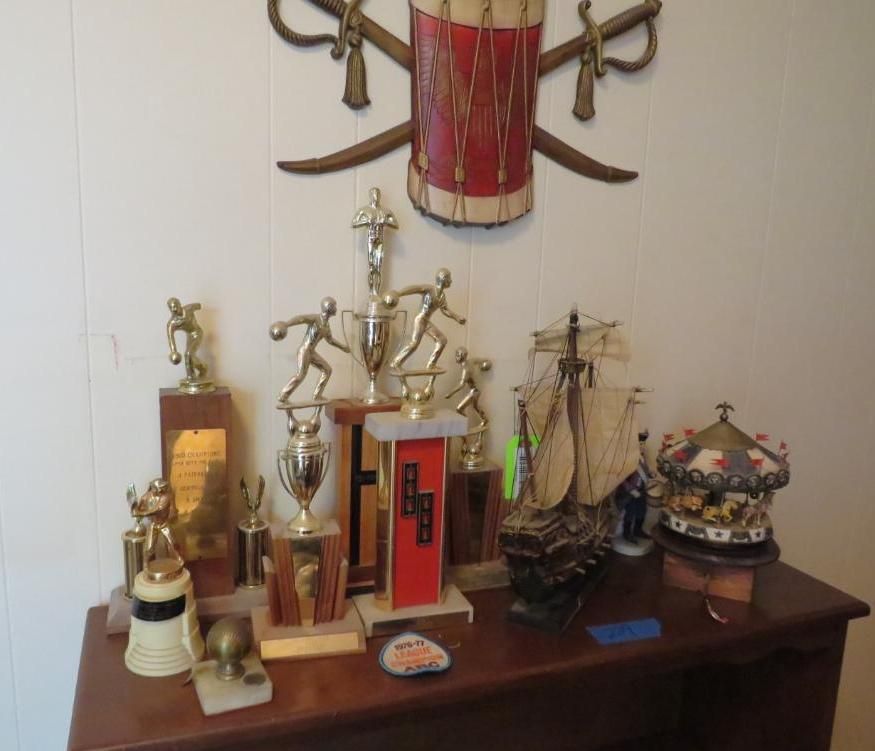 Trophies, model ship, and a carousel on a wooden table, with drum and crossed swords decoration on the wall.