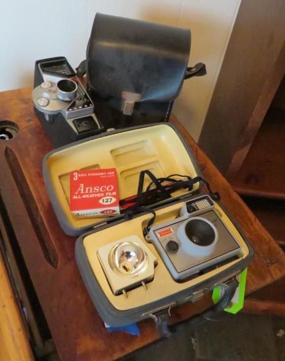 Vintage cameras and accessories on a wooden surface, including a flash and film.