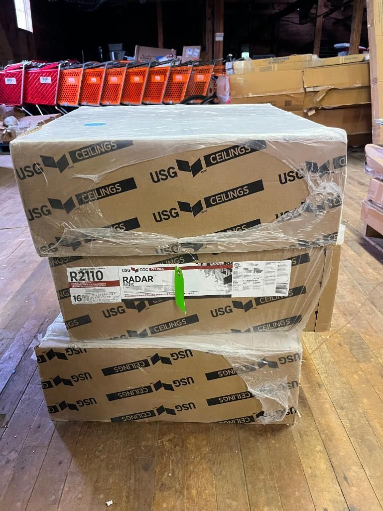 Three stacked cardboard boxes wrapped in plastic, USG brand, indoors on wood floor.