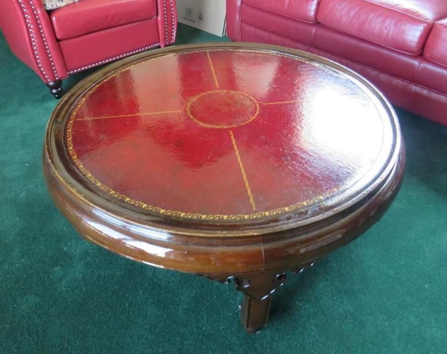 Round coffee table with red leather top and wooden base.