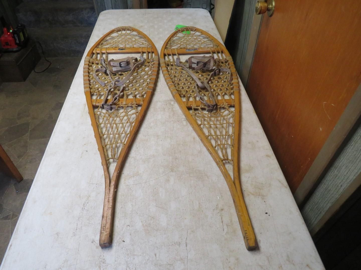 Two wooden snowshoes with woven webbing, lying on a white surface.