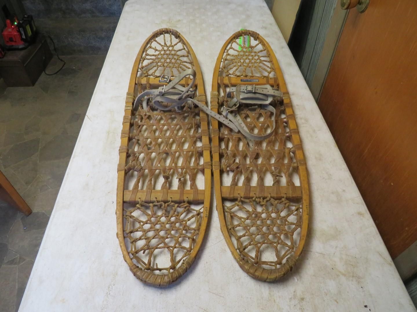 Pair of antique wooden snowshoes with woven webbing and leather straps, on a white surface.