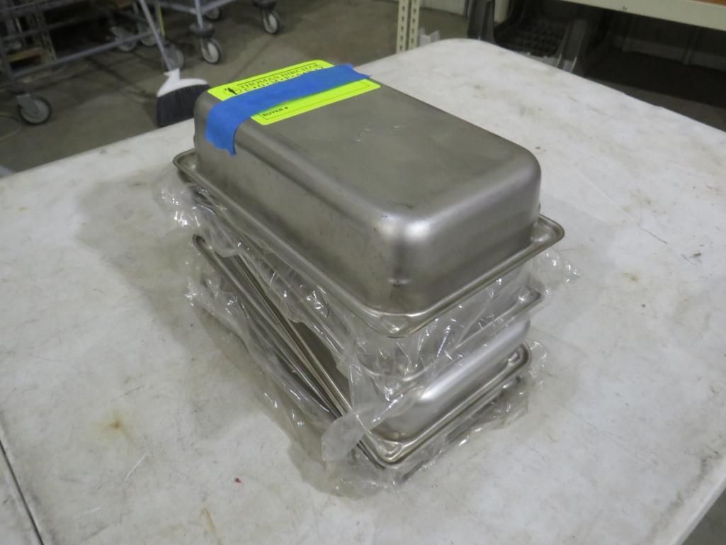 Stack of stainless steel food pans wrapped in plastic on a table. Blue and yellow tape on top pan.