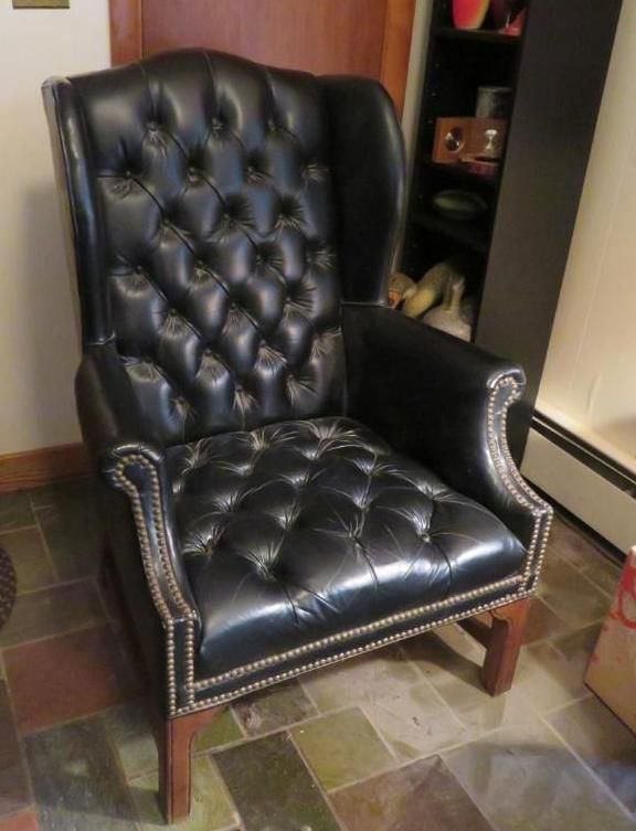 Black leather wingback chair with button tufting and studded trim.