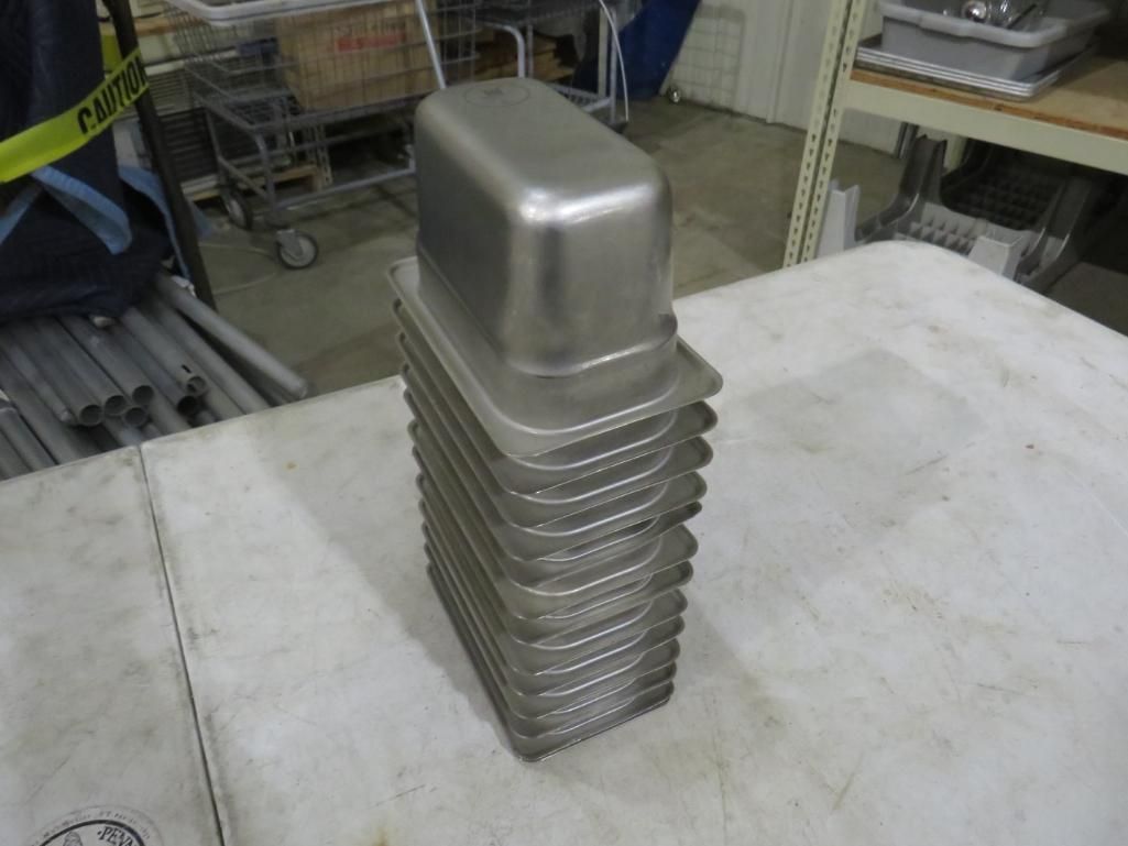 Stack of stainless steel food containers on a white table; industrial setting.
