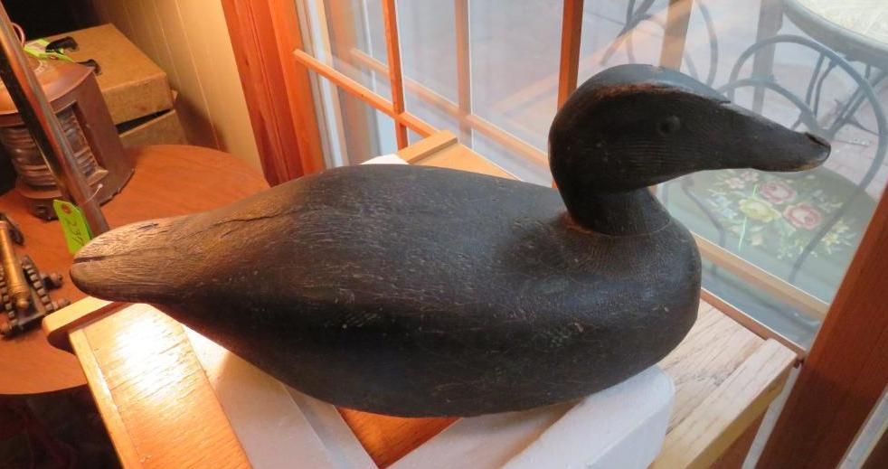 Black wooden duck decoy sitting on a white surface, near a window.