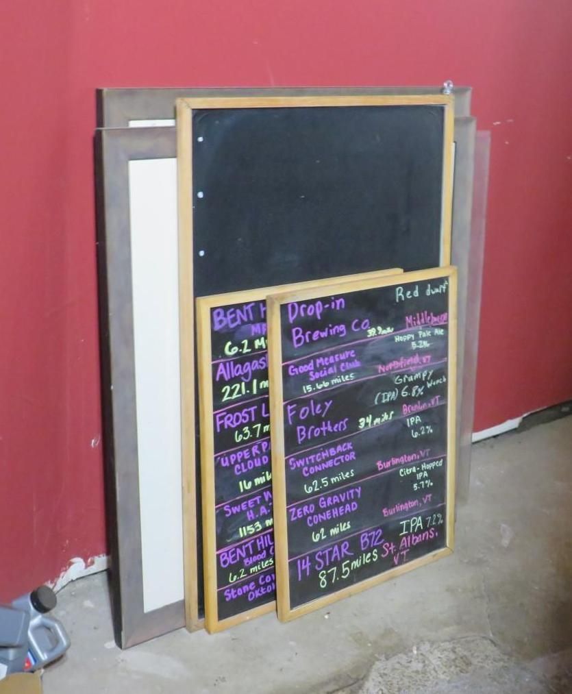 Blackboards with beer menu leaning against a red wall.