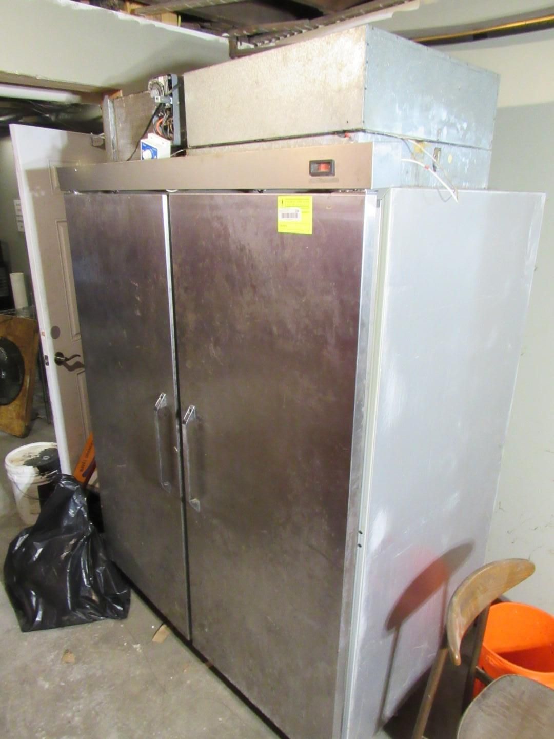 Two large, stainless steel commercial refrigerators in a basement setting.
