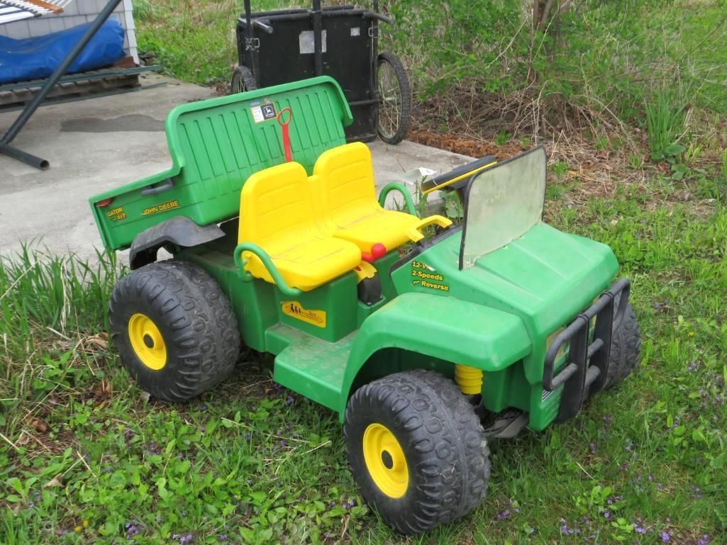 Green and yellow John Deere Gator ride-on toy parked on green grass.