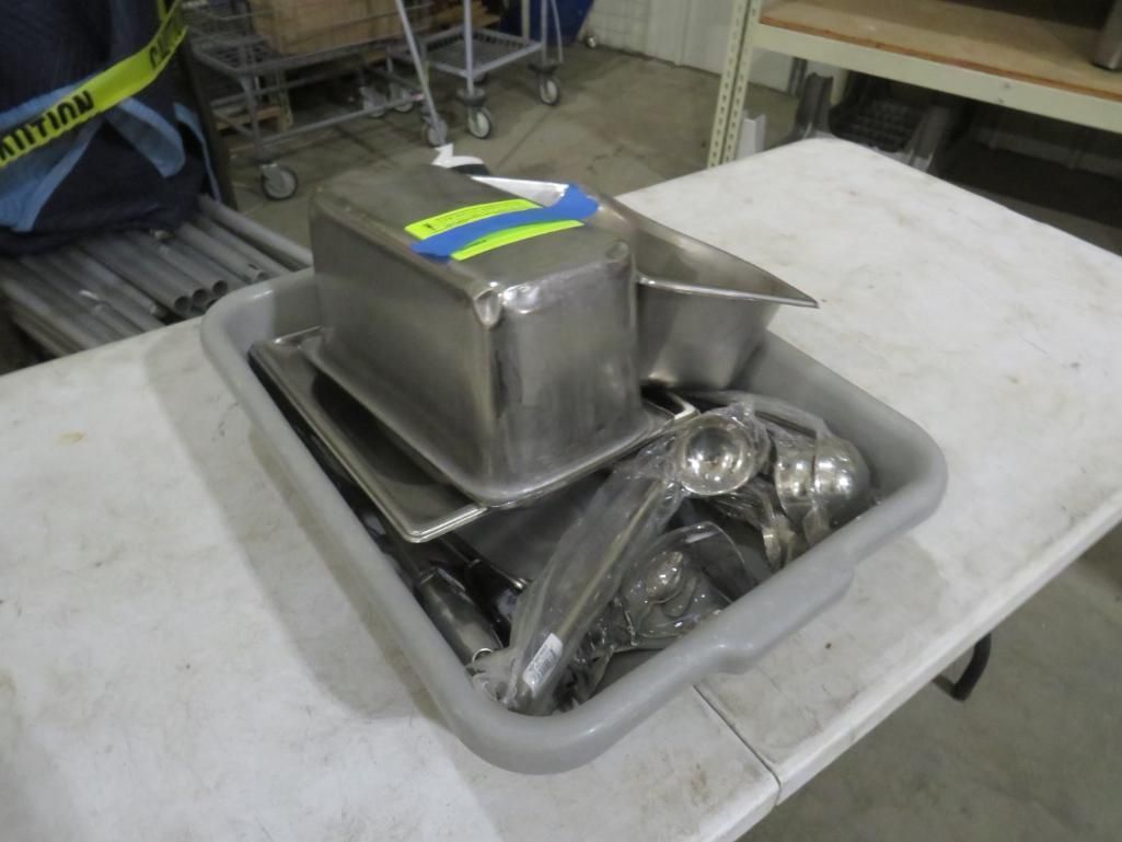 Tray of stainless steel food containers, serving utensils on a white folding table.
