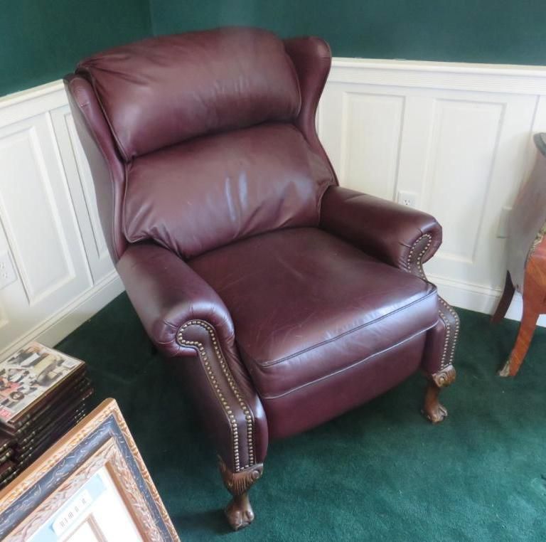 Burgundy leather recliner chair with nailhead trim and wooden claw feet, in a room with green carpet.