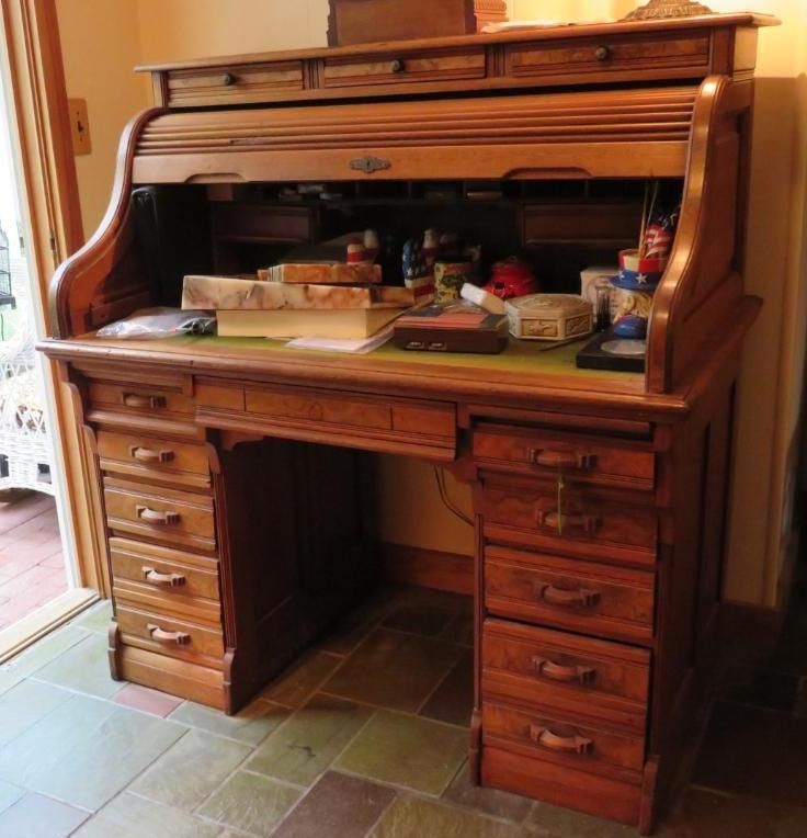 Wooden antique roll-top desk with drawers and upper storage. The desk sits indoors with items on the desktop.