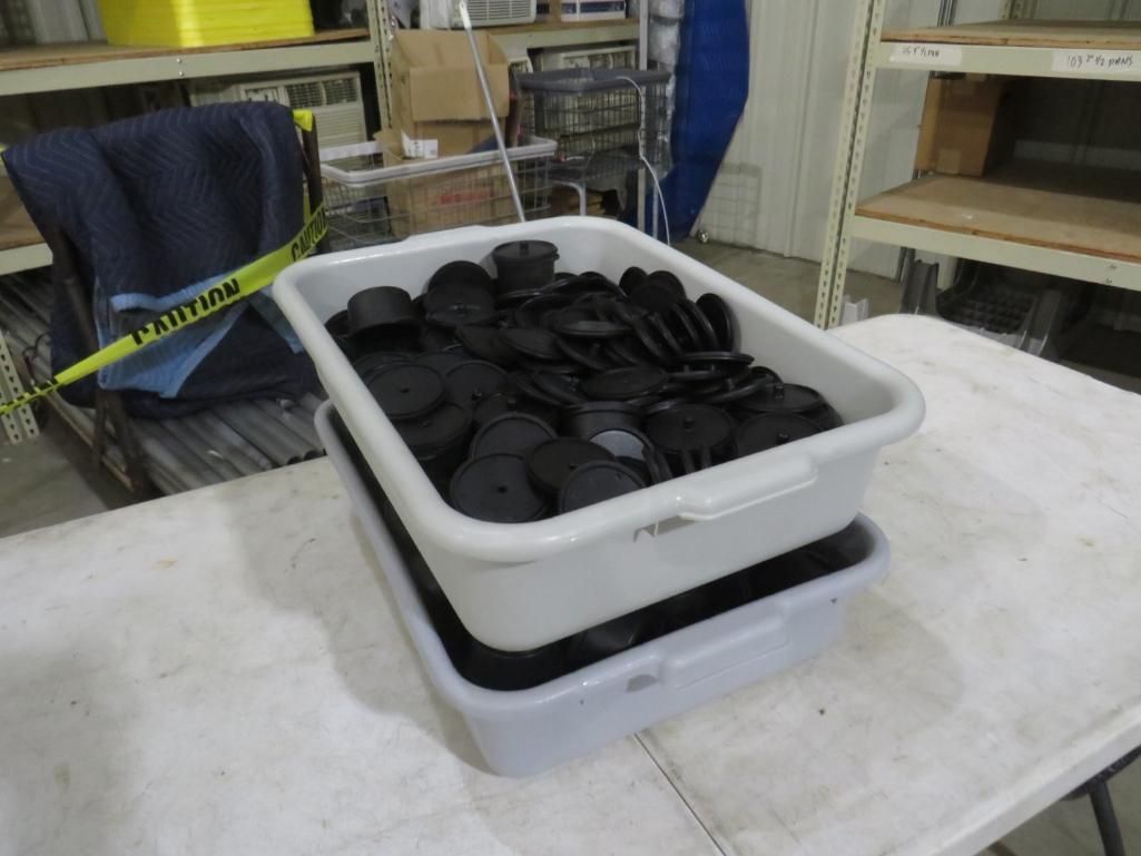 Two white plastic bins stacked on a table. The top bin holds black rubber pieces. Warehouse setting.