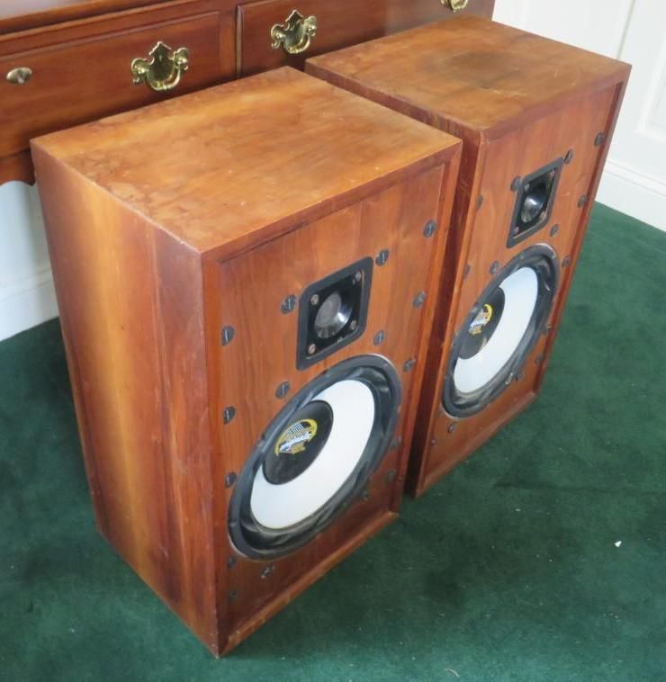 Two wooden speakers with black and white speaker components on green carpet.