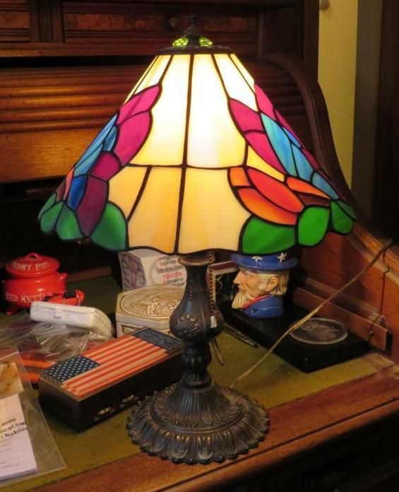 Stained glass lamp with a colorful bird design sits on a desk with various items.