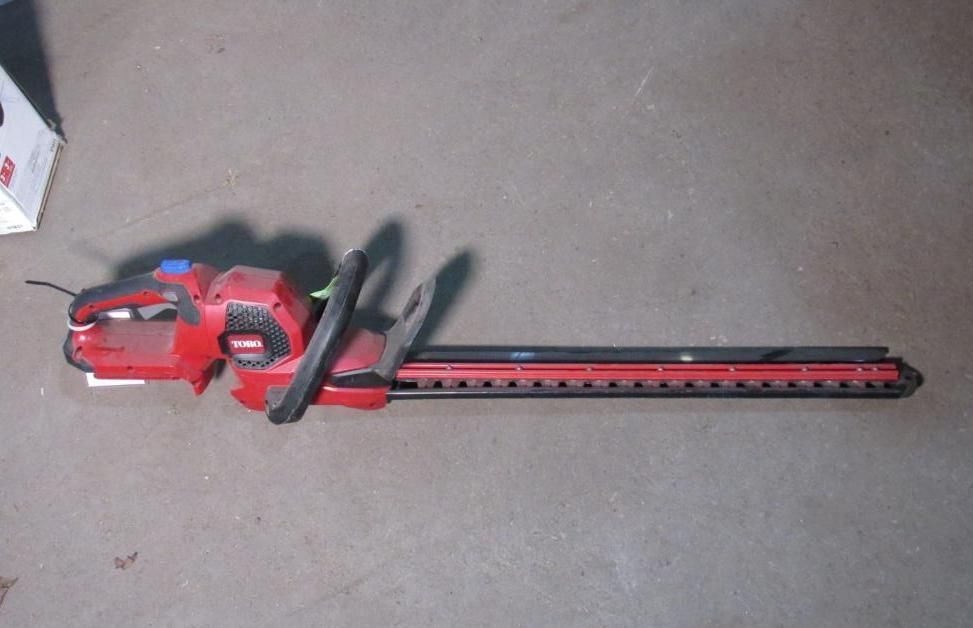 Red and black hedge trimmer on a concrete surface.