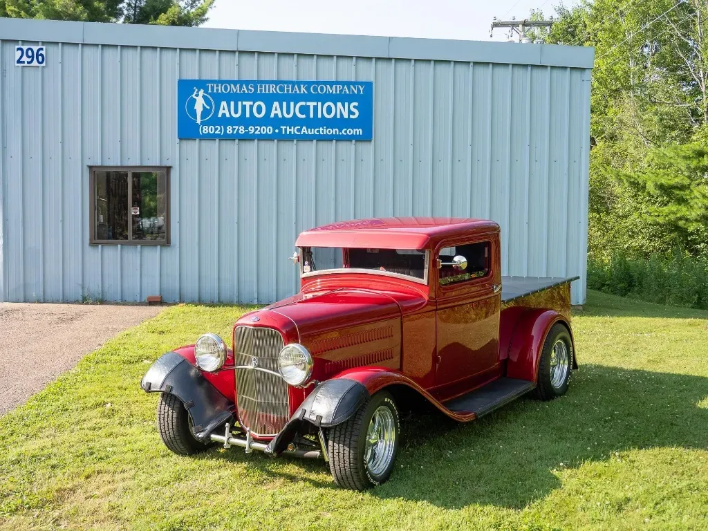 Red classic pickup truck parked in front of an auto auction building.