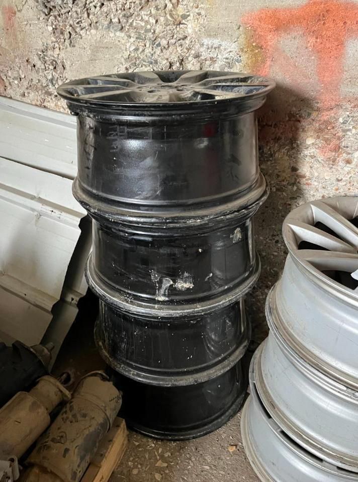 Four stacked black car rims, next to other rims.