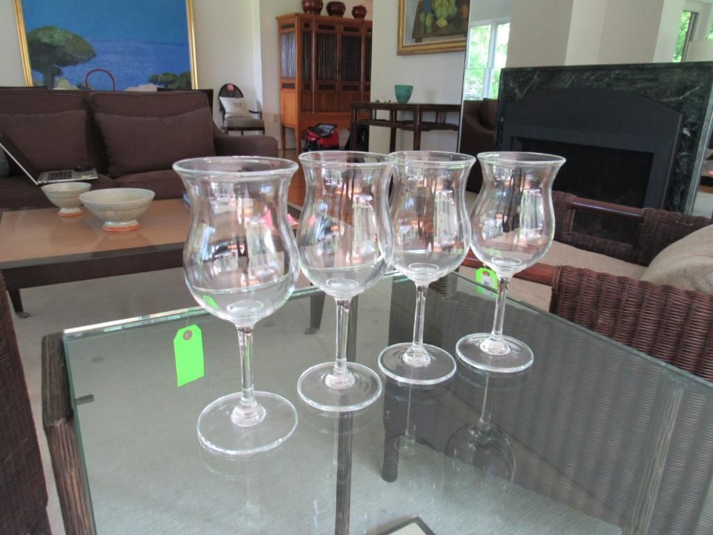Four clear stemmed glasses on a glass table in a living room.