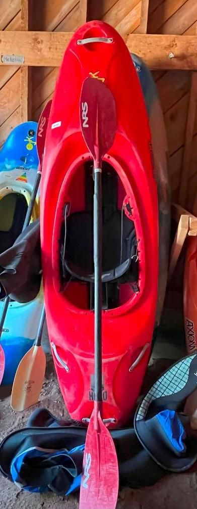 Red kayak with paddle, stored indoors. Other kayaks and gear are visible.