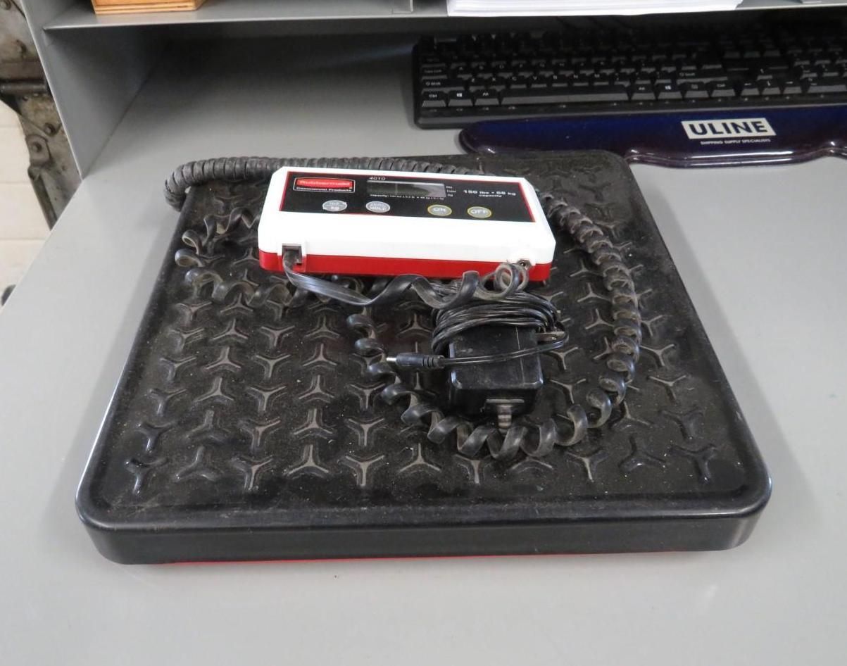 Black and red shipping scale with a control panel and coiled cable on a textured surface.
