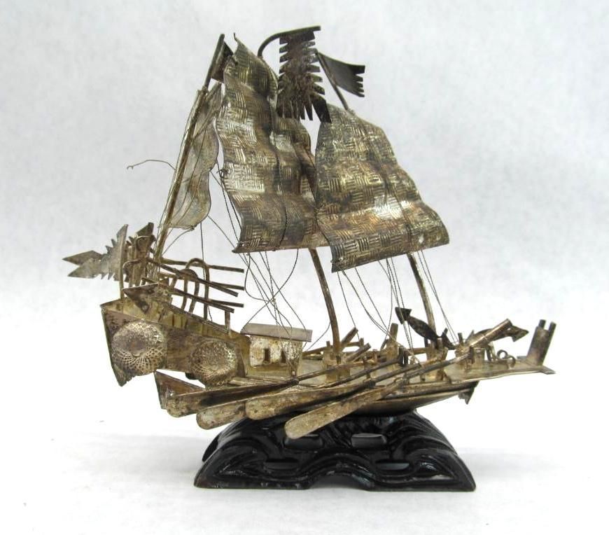 Silver metal sailboat sculpture on black wavy base.
