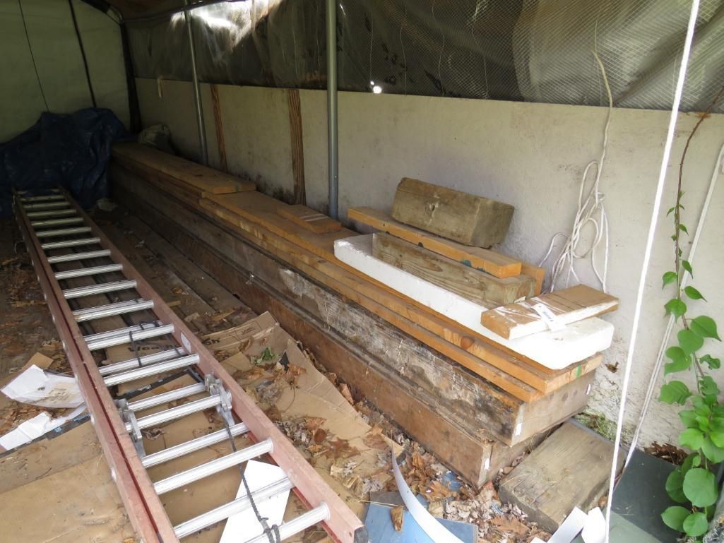 Stacked lumber and various materials in a covered outdoor area.