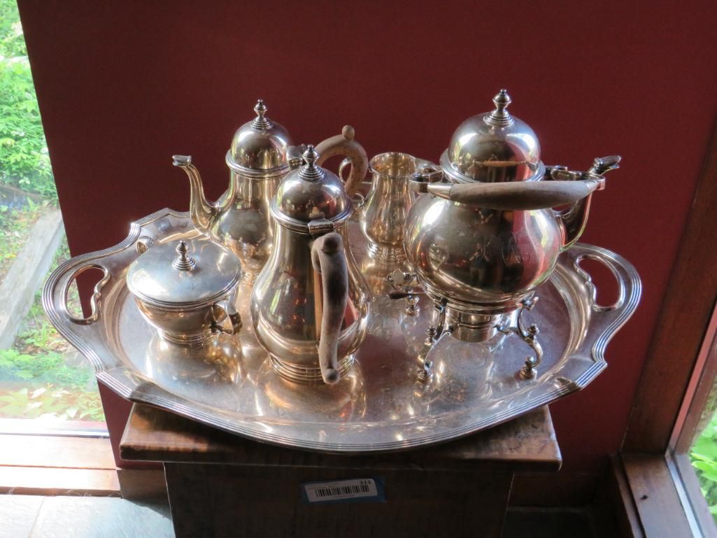 Silver tea set on an ornate tray, including a teapot, creamer, sugar bowl, and coffee pot, displayed on a wooden surface.