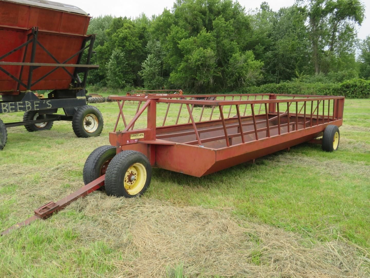 Red hay wagon on a grassy field with a second wagon visible in the background.