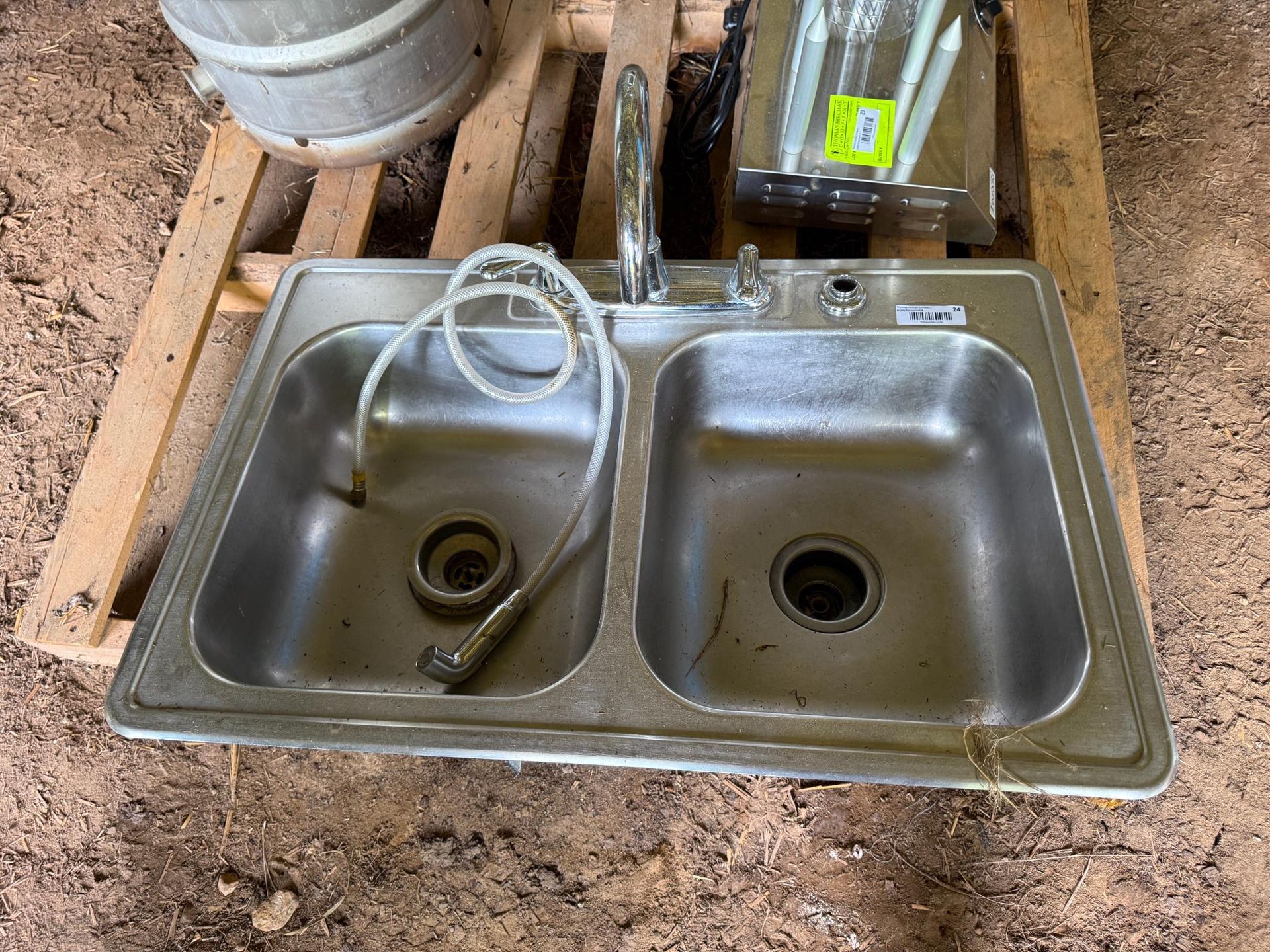 Stainless steel double sink with faucet and sprayer on a wooden pallet.