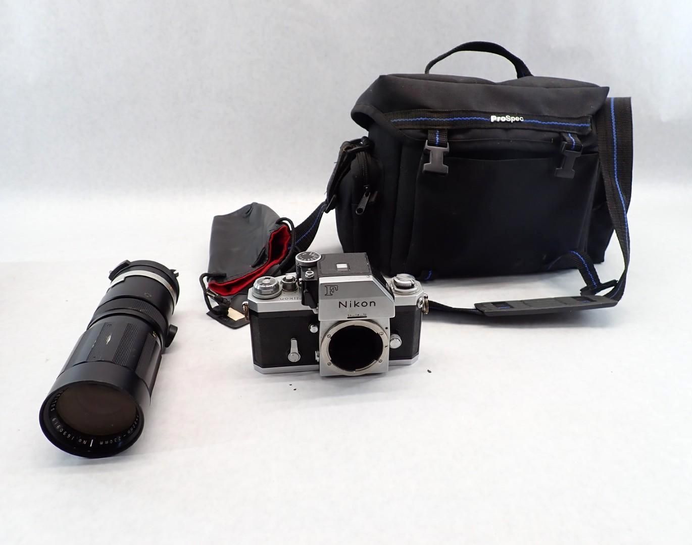 Black camera bag, film camera, and telephoto lens on white surface.