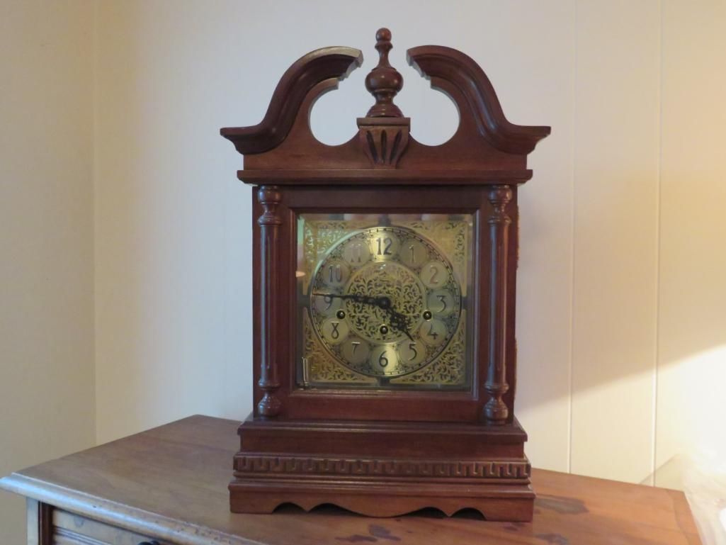 Wooden antique clock on a wood surface, with a glass face displaying the clock mechanism.