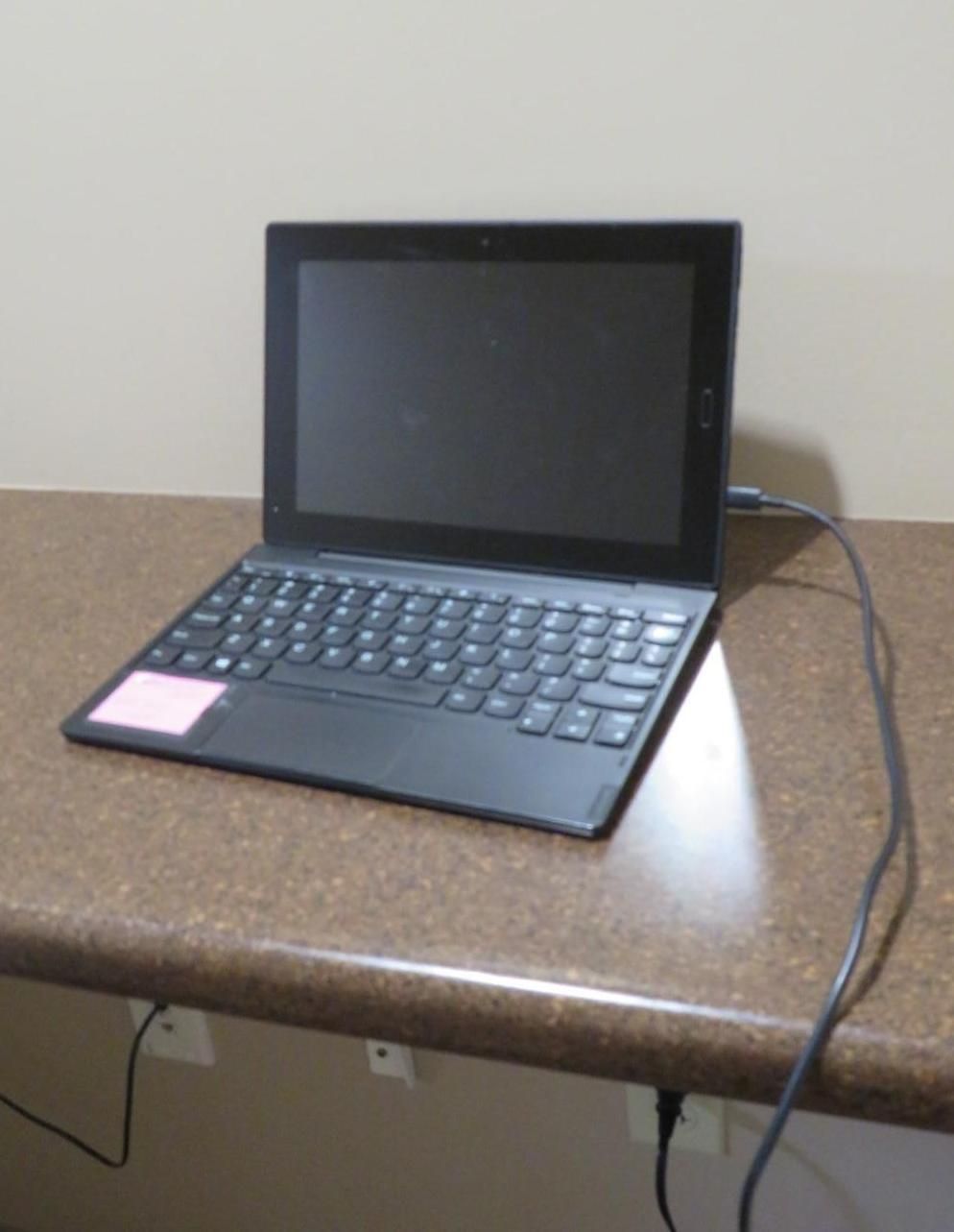 Black laptop on a brown countertop, plugged into a wall outlet.