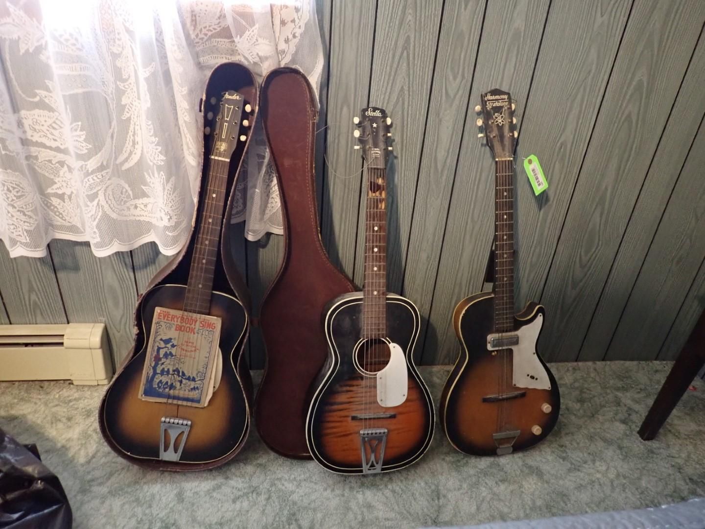 Three vintage guitars with cases against a paneled wall, varying wood tones.