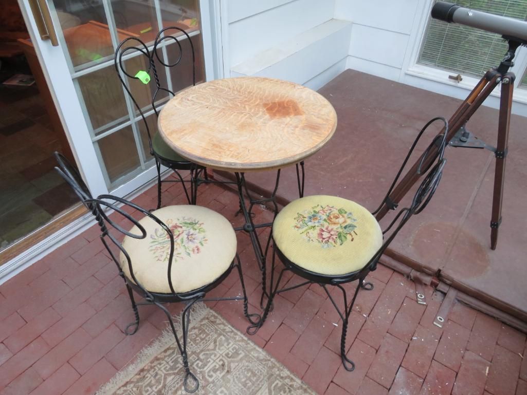 Wrought iron bistro set with round table and two floral-cushioned chairs, on a porch with telescope.