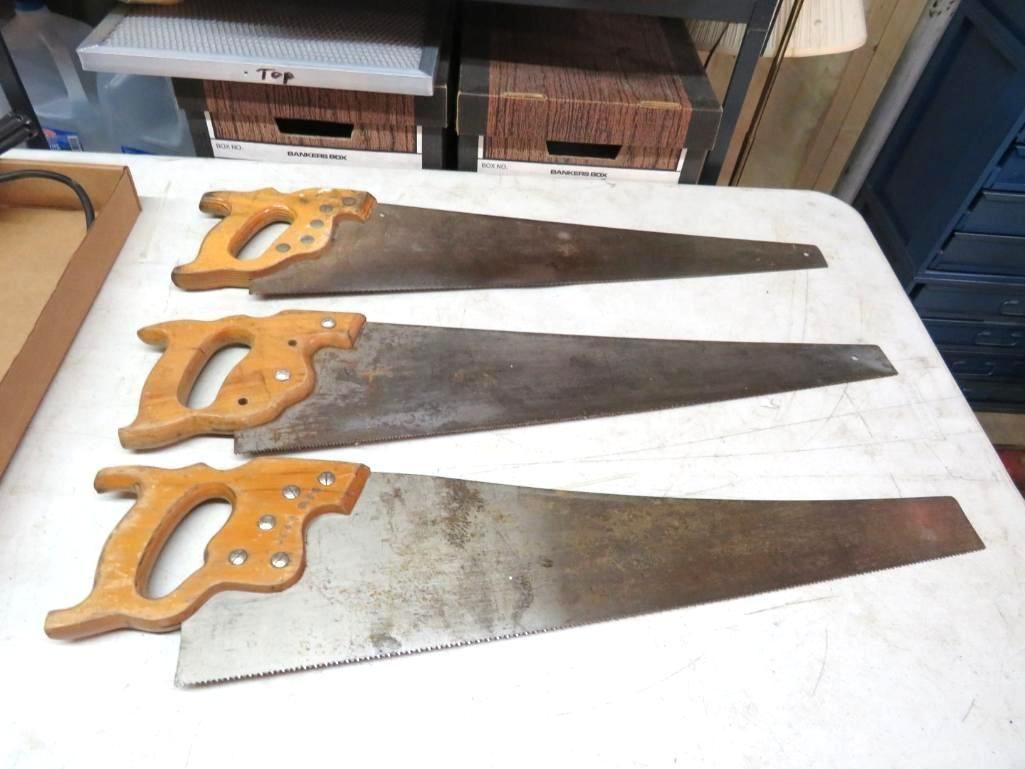 Three vintage hand saws with wooden handles on a white surface.