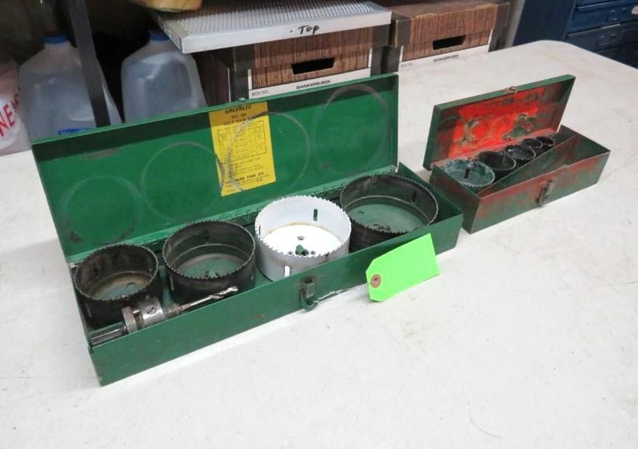 Two green metal hole saw toolboxes open on a white surface. One red toolbox is next to it.