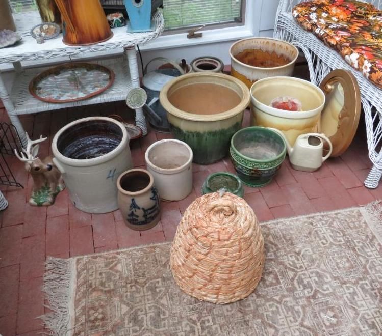 A collection of terracotta pots and a woven beehive on a brick patio, near a wicker chair and a shelf.