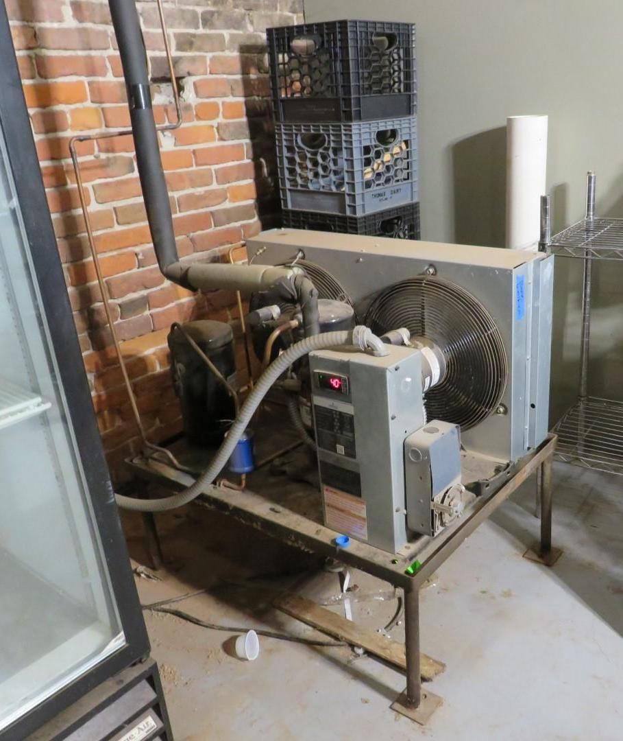 Industrial refrigeration unit on metal frame, against brick wall.