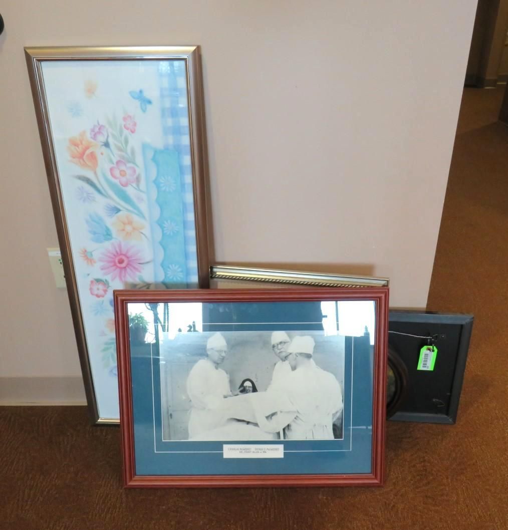 Four framed items: floral art, a sepia-toned group, and two smaller frames, leaning against a pink wall.