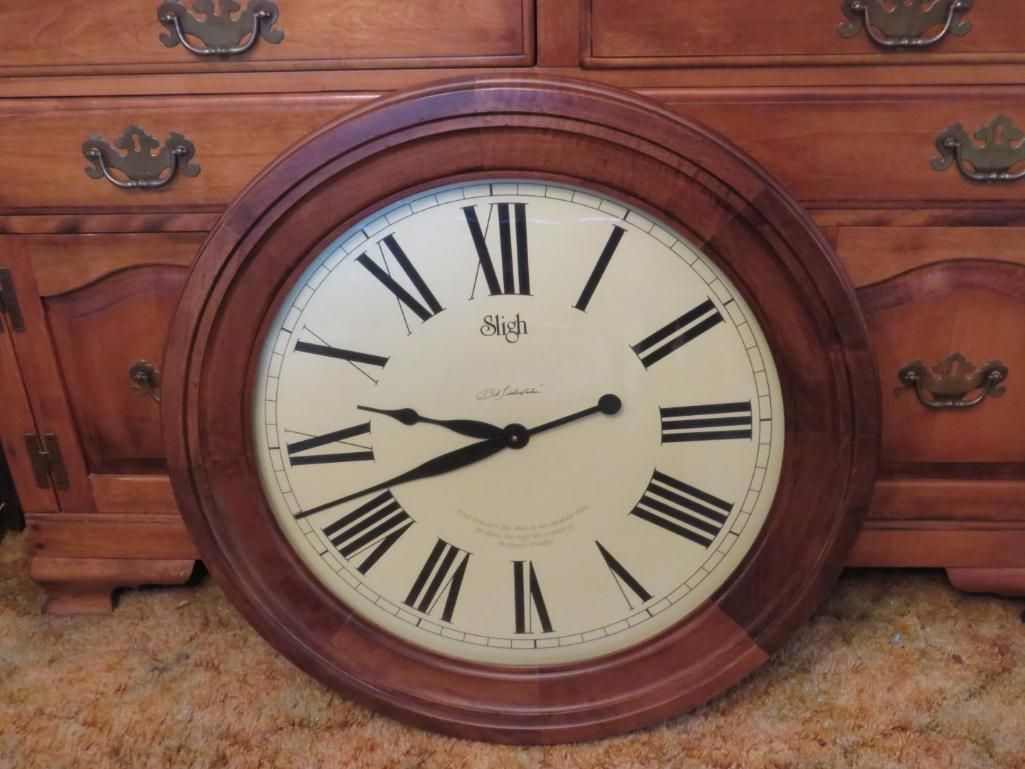 Wooden clock with Roman numerals, hands at 2:40, set against a wooden dresser.