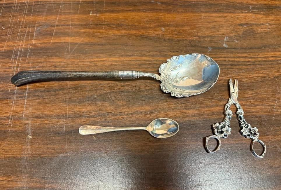 Three silver utensils on a wood surface: a large spoon, a small spoon, and sugar tongs.