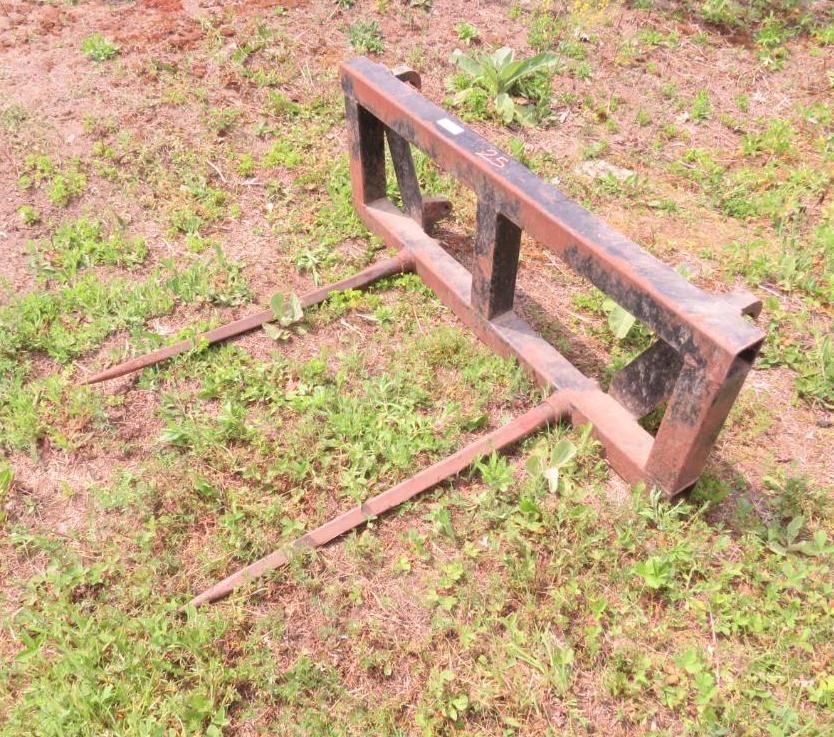 Metal hay bale spear attachment resting on grassy ground.