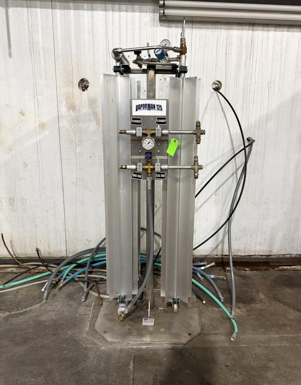 Industrial equipment with clear tubes, gauges, and hoses against a white wall and concrete floor.