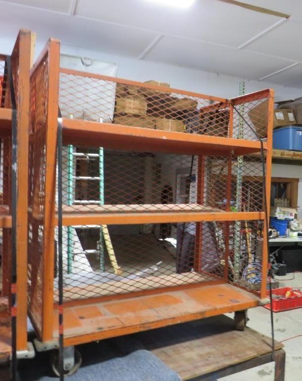 Orange rolling cart with wire mesh sides, three shelves, and stacked boxes on top.