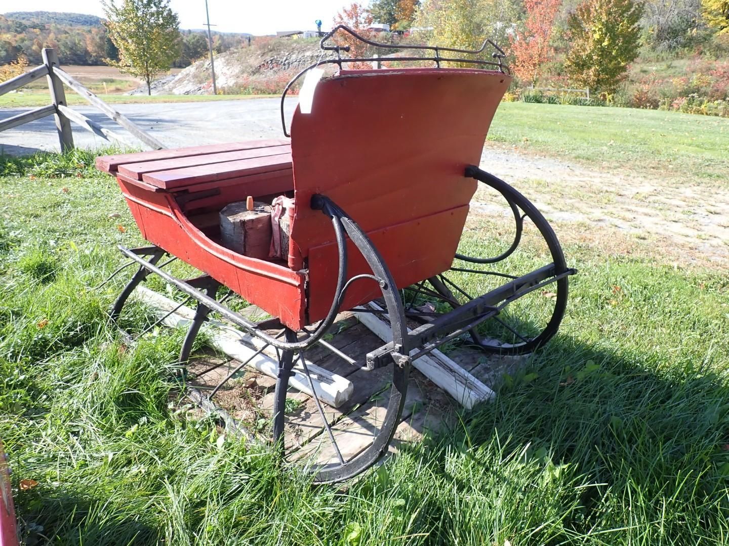 Red wooden sleigh with black runners on a grassy path outdoors in autumn